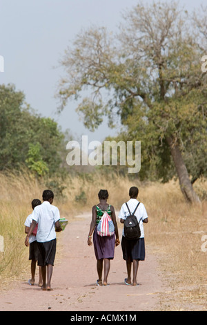 School girls in uniform with back packs walk home on dusty track near Tendaba The Gambia Stock Photo