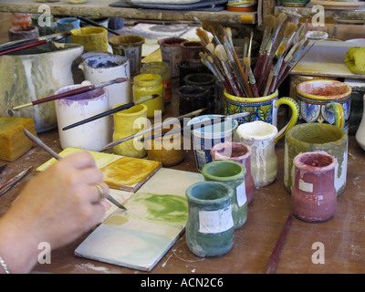 Hand holding paint brush dips into fresh paint in the process of painting ceramics designs ceramics factory in Deruta Italy Stock Photo