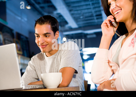 young couple using laptop and mobile phone in internet cafe Stock Photo
