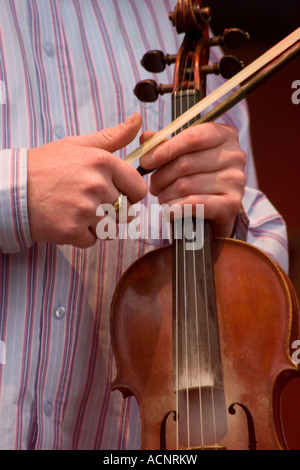 Man in striped shirt holding violin and bow on stage at Irish traditional music concert Stock Photo