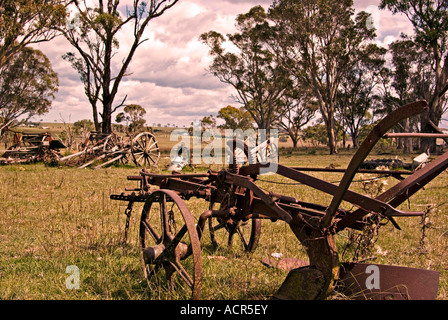 an old rusting horse drawn plow sits in the farm paddock surrounded by other broken equipment Stock Photo