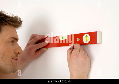 Young man using spirit level, marking with pencil on wall, smiling Stock Photo