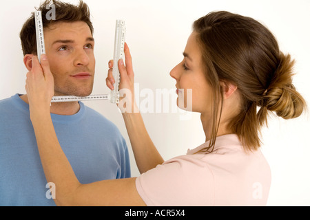 Woman measuring man's face with ruler, smiling, close-up Stock Photo