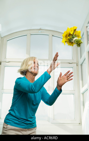 Senior woman catching bunch of flowers, smiling, low angle view Stock Photo