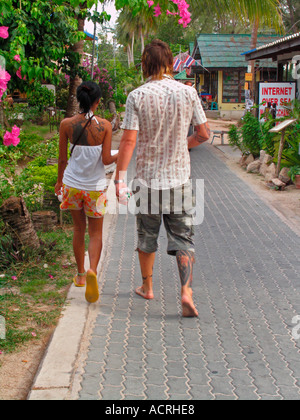 Couple with tattoos stroll on paved walkway along beach at Hat Sai Ri on island of Ko Tao Thailand Stock Photo