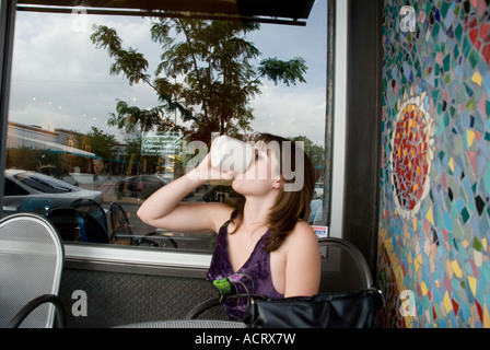 A young woman sips her coffee and talks on the phone as she relaxes in a small coffee shop located in Albuquerque, New Mexico Stock Photo