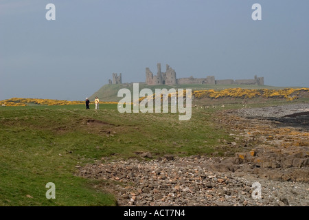 two elderly ladies walking near dunstanbutgh castle which can be seen through the mist in the background Stock Photo