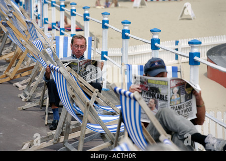 Two men reading newspapers sitting in deck chairs in Weymouth UK Stock Photo