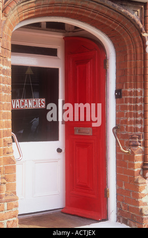 Front porch of small hotel or guest house with elaborate carved brickwork fresh painted red door and sign stating Vacancies Stock Photo