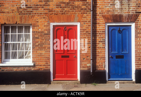Detail of a Georgian house terrace showing fancy orange brickwork sash window with curtain closed and red and blue doors Stock Photo