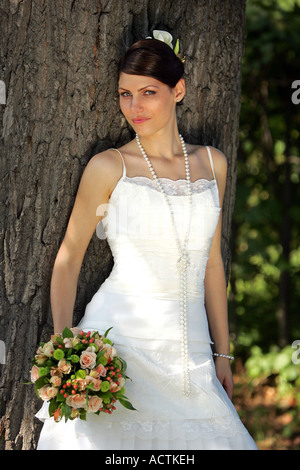 Portrait of a Bride stood next to tree with bouquet smiling Stock Photo
