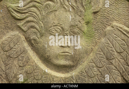 Detail of the head and wings of a disembodied angel carved in a naive style on a weathered sandstone gravestone Stock Photo