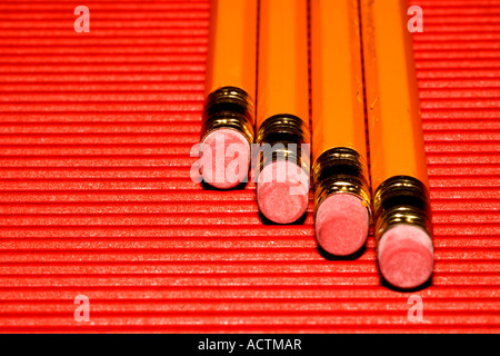 4 yellow pencils with erasers at the tip on a red corrugated surface Stock Photo