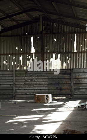 A refridgerator lies on its side in an old empty and rundown barn with the sun shining through holes in the roof and graffiti Stock Photo