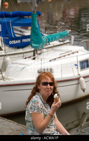red haired young smiling woman eating ice cream by Aberaeron harbour summer 2007 during the seafood festival Stock Photo