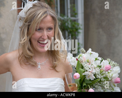 Young english bride on her wedding day with bouquet glass of champagne, wedding dress and bridal veil looking happy and smiling Stock Photo