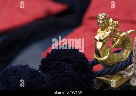 detail of a gondola in Venice Italy showing a bronze mermaid cleat purple rope and pompom and red cushions Stock Photo