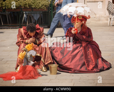 two Venician street performers in traditional Renaissance costume sitting on the Riva Degli Schiavoni waterfront taking a cigare Stock Photo