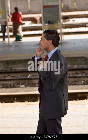 Editorial use only No model release young Italian business man talking on cell phone on train platform in Italian train station Stock Photo