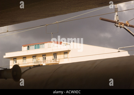 sunlit apartment building in Messina Sicily from train station over top of train roof and below ceiling of the train platform Stock Photo