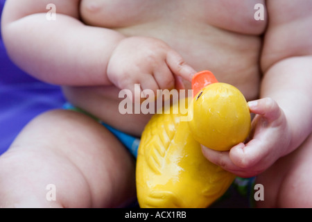 Baby in wading pool pointing to mouth of toy duck. Stock Photo