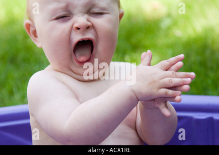 Happy baby in wading pool, clapping her hands in glee. Stock Photo