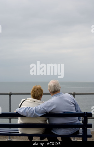 an elderly couple sitting on a bench by the sea and looking out over Cardigan Bay, Aberystwyth Ceredigion, grey overcast day UK Stock Photo