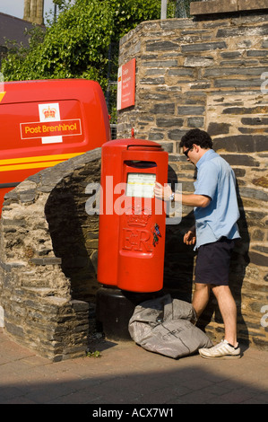 Postman collecting emptying the mail post from a post box outside Cardigan postal depot wales (logo in welsh on van behind) Stock Photo