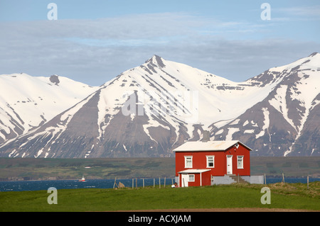 Small red cottage on the shore of Eyjafjördur with snow capped mountains on the background, North of Dalvik, Iceland Stock Photo