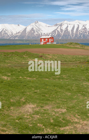 Small red cottage on the shore of Eyjafjördur with snow capped mountains on the background, North of Dalvik, Iceland Stock Photo