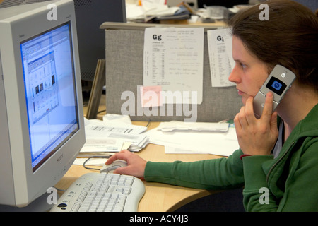 Office worker using a computer and cell phone. Stock Photo