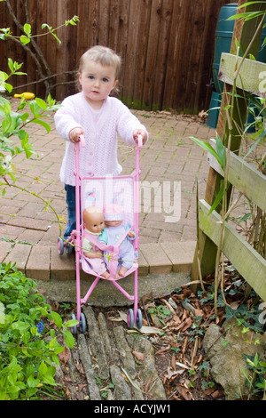 Little girl pushing a baby doll around the garden in a pushchair buggy Stock Photo