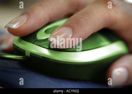 Womans hand using a green computer mouse with scroll wheel in an office to illustrate green and environmental computing issues Stock Photo