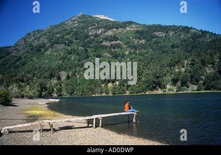 Latina girl sitting on rustic wooden jetty looking at view, Lake Paimun, Lanin National Park, Neuquen Province, Argentina Stock Photo