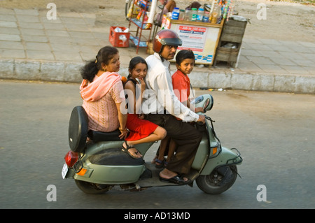 Horizontal aerial view of an entire Indian family on one tiny moped travelling along the road at speed in central Delhi. Stock Photo