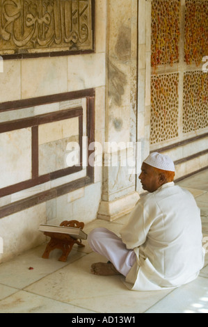 Vertical close up of an Indian man sitting at an inscription on a wall reading from a prayer book inside Salim Chisti's tomb. Stock Photo