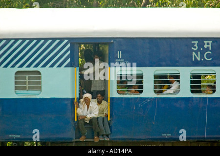 Horizontal close up of local Indian men sitting on the doorstep of a moving train. Stock Photo