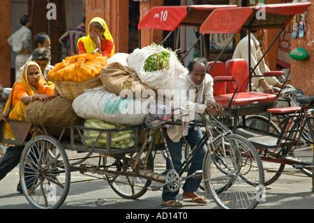 Horizontal portrait of a cycle rickshaw piled high with sacks of produce and two old women, being pushed along by an Indian man. Stock Photo