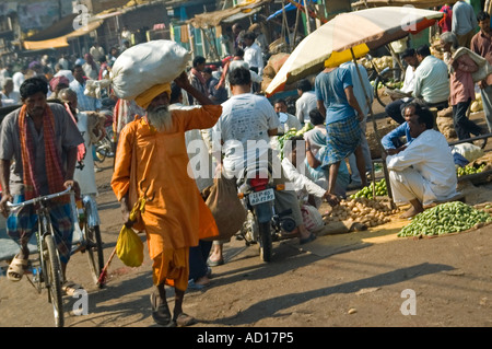 Horizontal wide angle of a typical busy Indian streetscene with a man carrying a big bundle on his head walking along the road Stock Photo