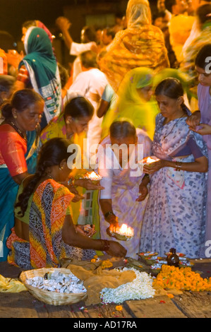 Vertical close up of Indian women buying flower garlands and candles 'diyas' during the religious prayers 'aarti' on the Ganges. Stock Photo