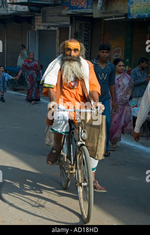 Vertical portrait of an Indian Sadhu 'holy man' cycling through the streets of Varanasi on a rickety old bicycle. Stock Photo