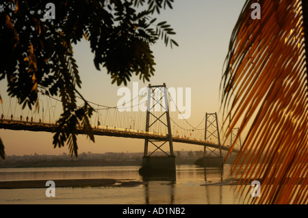 Suspension bridge over the Zambezi Zambeze River Mozambique at Tete at sunrise framed by palm fronds and tropical tree Stock Photo