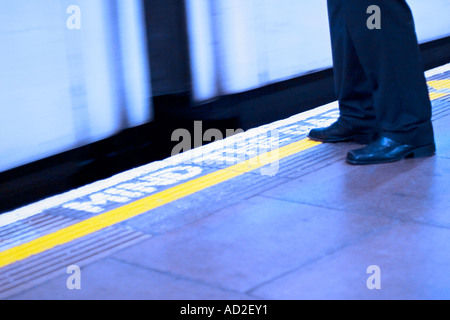 Young businessman stands on London Underground platform as tube train enters station Stock Photo