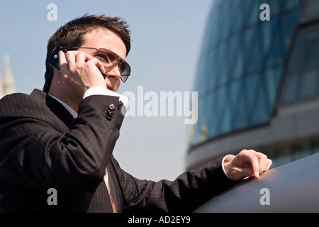 Young businessman rests on railing whilst using mobile phone in More London Place development near City Hall London Stock Photo