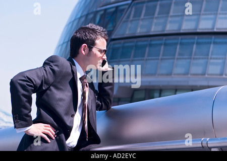 Young businessman rests on railing whilst talking on mobile phone in More London Place development near City Hall London Stock Photo