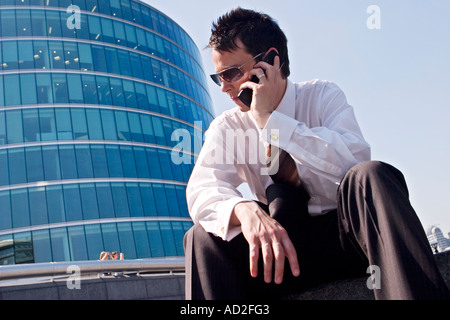 Young businessman sits down whilst using mobile phone More London Place development near City Hall London Stock Photo