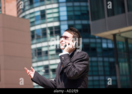 Young businessman looking up smiling as he uses mobile phone in the City of London Stock Photo