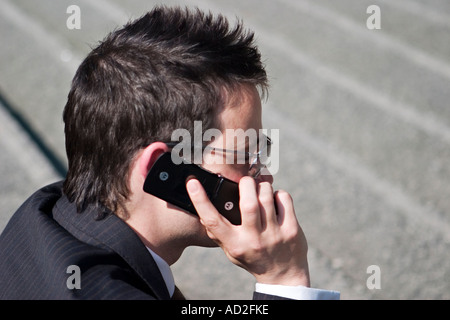 Young businessman sitting on steps as he uses mobile phone in the City of London Stock Photo