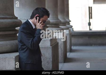 Young businessman looking down as he uses mobile phone in the City of London outside the Royal Exchange Stock Photo