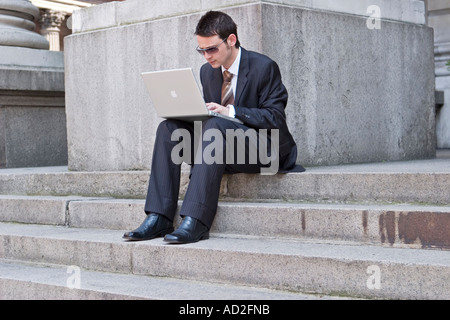 Young businessman looks at financial data on his laptop in the City of London Stock Photo
